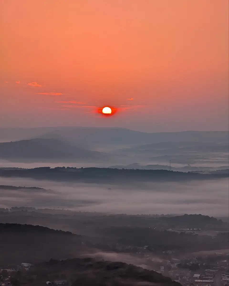 A red sunrise over misty Central Pennsylvania ridges, with fog filling the valleys and a distant tower.