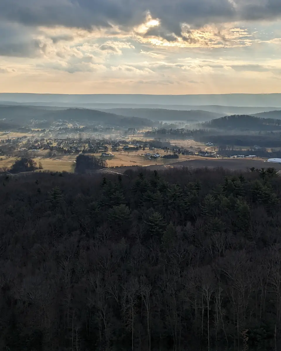 Golden evening light over a Central Pennsylvania valley of farms and ridges, seen from a tower above the forest.