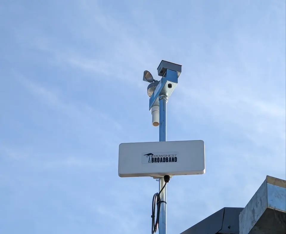 A Crowsnest radio and a security camera on a mast beside a commercial building.