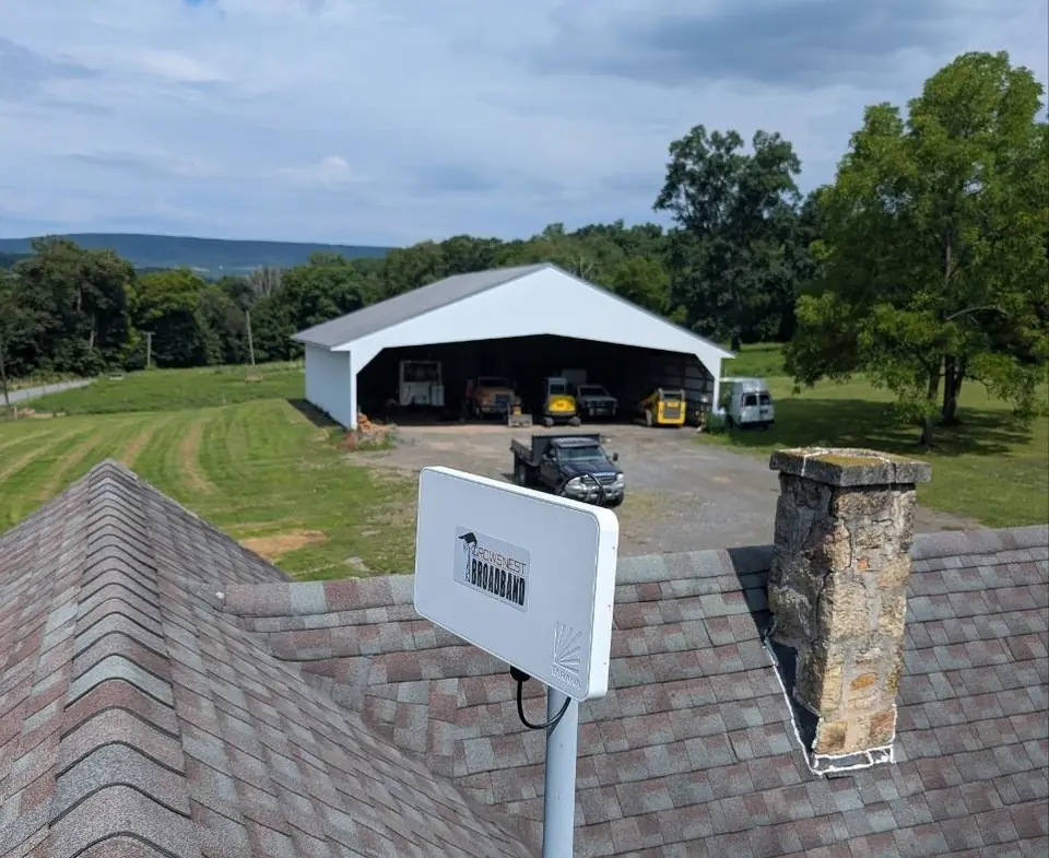 A Crowsnest radio on a roof mount beside a stone chimney, with a pole barn and lawn beyond.