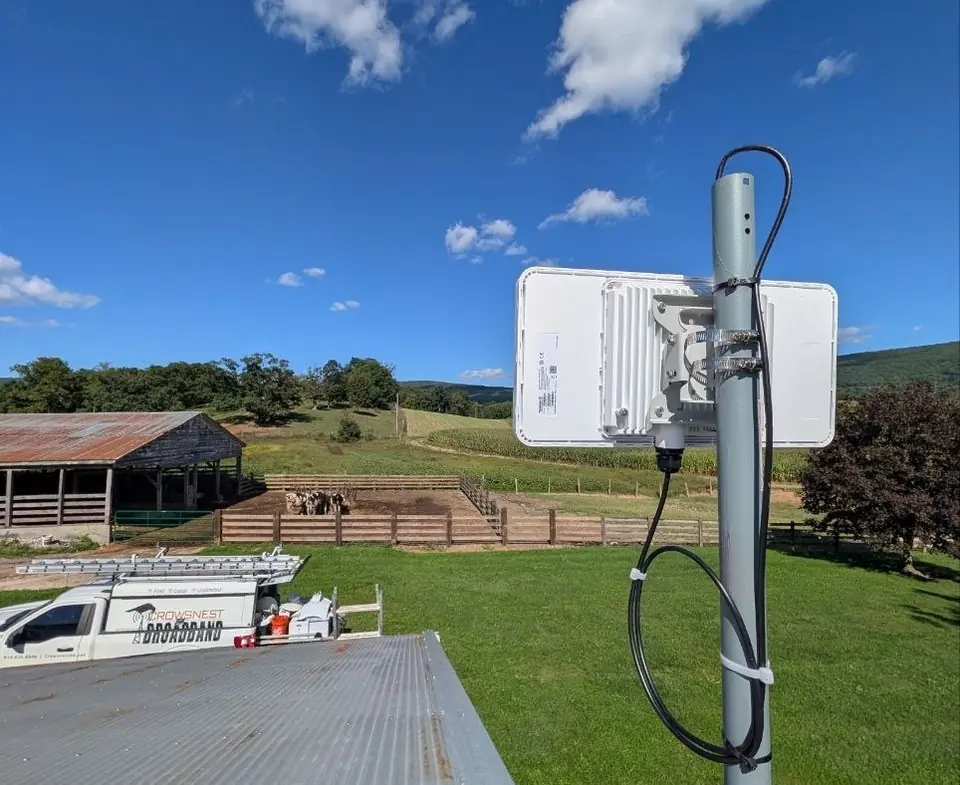 A Crowsnest radio on a farm roof above barns and pasture, with a Crowsnest service truck below.