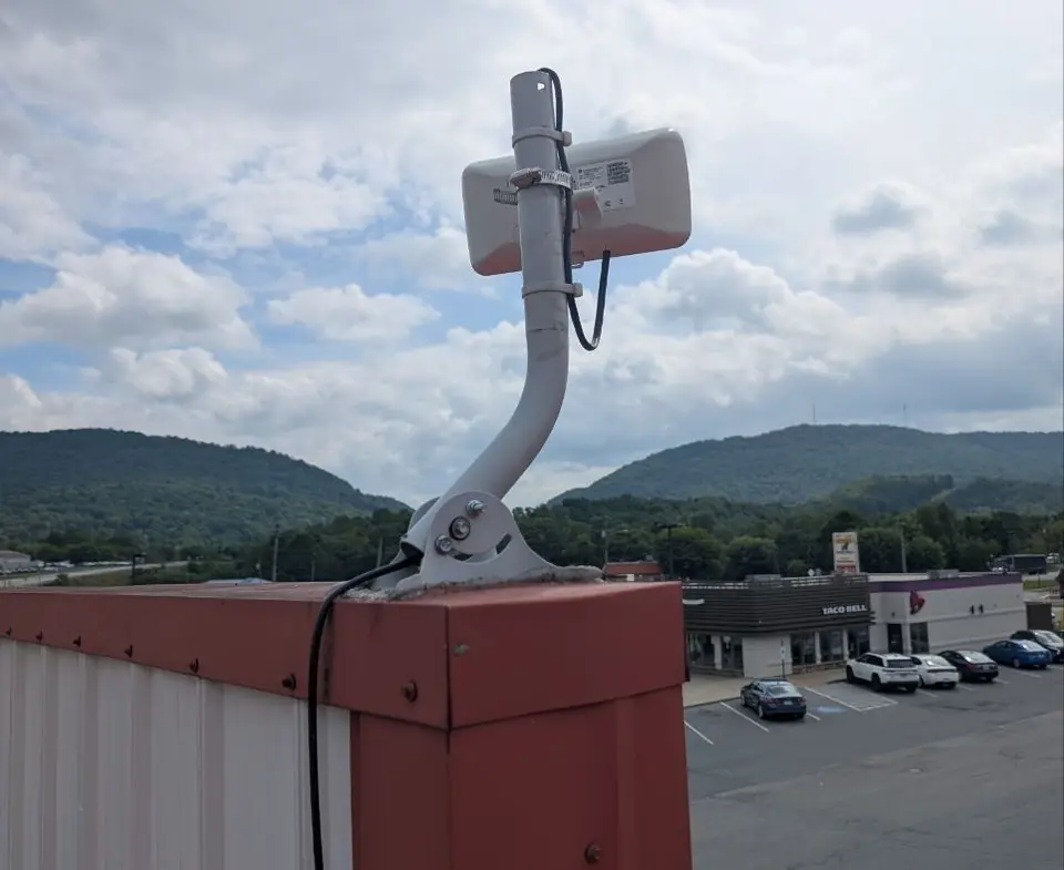 A compact customer radio on a mount atop a red commercial building, with wooded mountains beyond.
