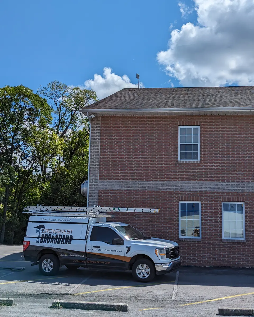 A Crowsnest Broadband pickup parked at a brick business building with a radio on its roof.