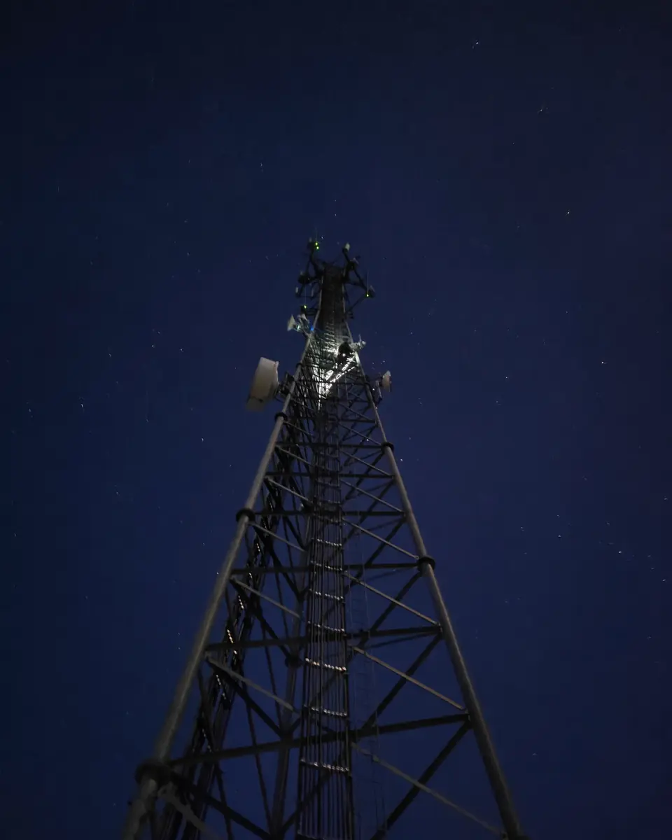 A lattice communications tower at night, its equipment lit against a dark, starry sky.